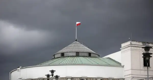 Polski parlament pod burzowym niebem. Biało-czerwona flaga powiewa na maszcie, symbolizując stan wyjątkowy w Polsce.