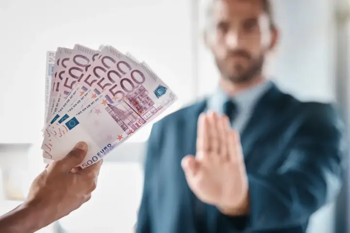 Ręka podaje plik banknotów 500 euro, mężczyzna w garniturze odrzuca je, co może symbolizować pozew o zapłatę.
